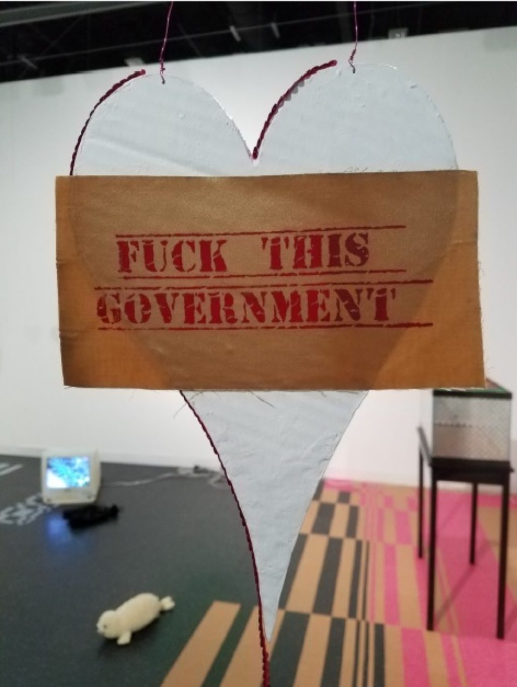Maggie Lee, Fthis.gov, 2016 gesso, modge podge, cardboard, laser photocopy, acrylic, wire, silkscreen on fabric Heart: 13 x 9 inches (33.02 x 22.86 cm),Sequined string: 79 inches (200.66 cm),Hanging wire: 54 inches (137.16 cm) Photo courtesy of the gallery.