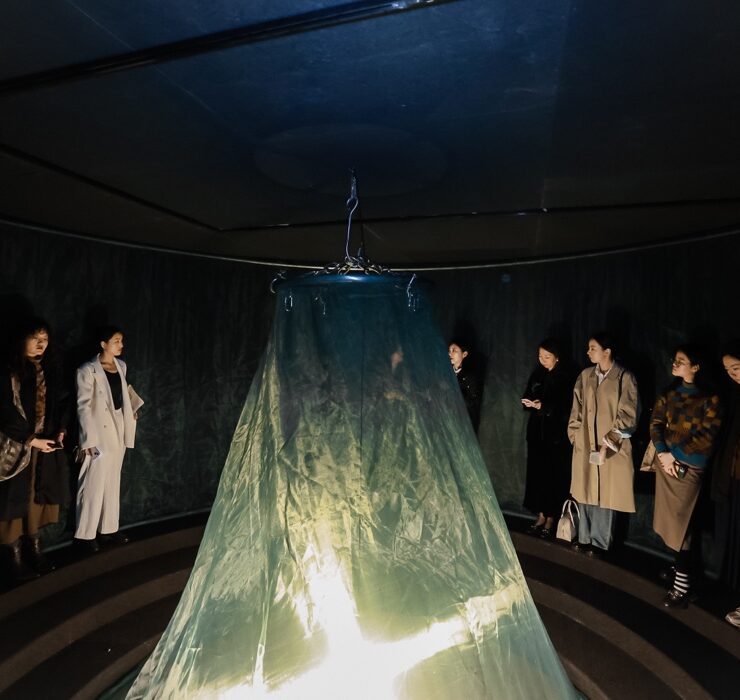 A group of people standing around a large green object Description automatically generated