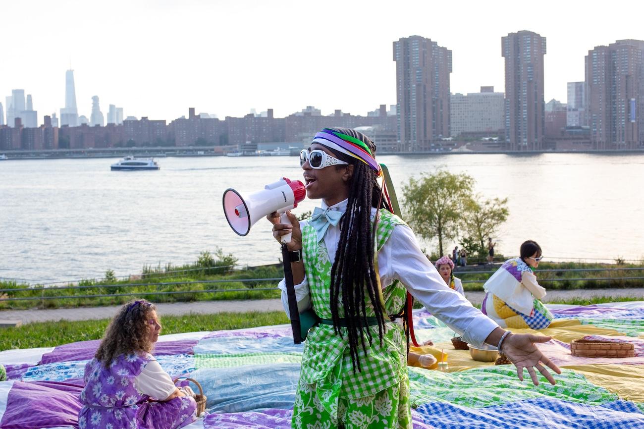 Fitzmore Codogan addresses the audience while Hsiao-Chu Hsia (Julia) dances in the background in “The Picnic: Harvest of the Soft Sweet Sound.” Photographed by Yann Chashanovski. Courtesy of Flux Factory.