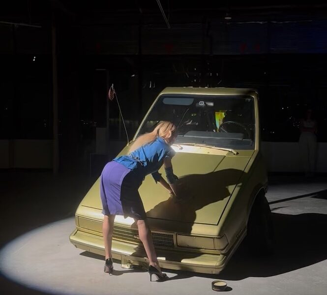 A person in a blue skirt and blue blouse leaning on a car AI-generated content may be incorrect.