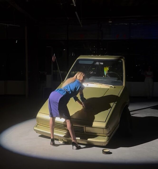 A person in a blue skirt and blue blouse leaning on a car AI-generated content may be incorrect.