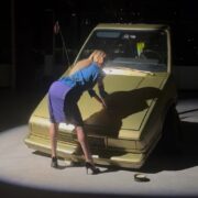 A person in a blue skirt and blue blouse leaning on a car AI-generated content may be incorrect.