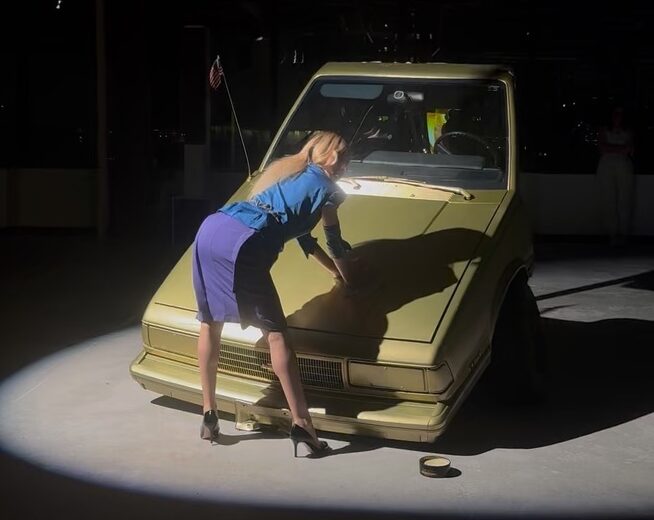 A person in a blue skirt and blue blouse leaning on a car AI-generated content may be incorrect.